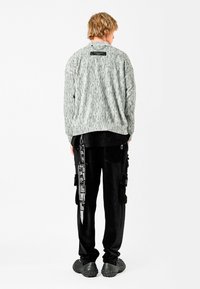 Suéter de punto gris jaspeado con cuello redondo, combinado con pantalones cargo negros que cuentan con múltiples bolsillos y una correa con gráficos impresos.