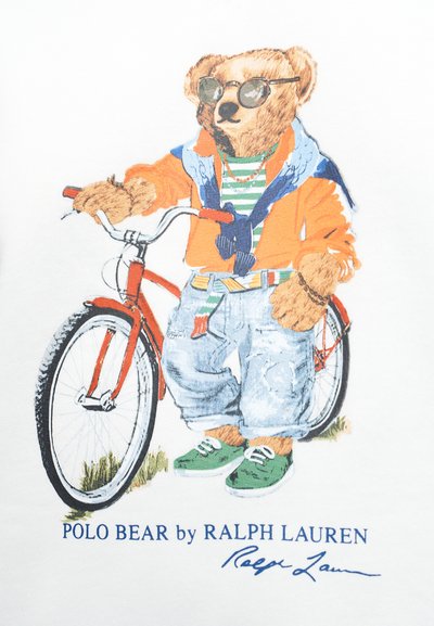 Bär mit Sonnenbrille, gestreiftem Hemd, orangefarbener Jacke, Jeans und grünen Schuhen steht neben einem roten Fahrrad.