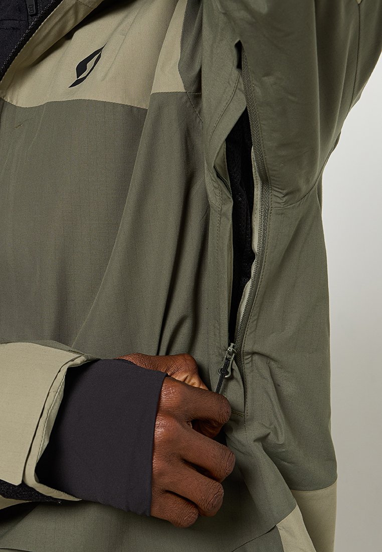 Chaqueta verde oliva con acentos beige, que cuenta con un bolsillo con cremallera y tela texturizada, costuras detalladas y mangas ajustadas.