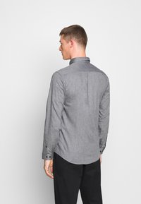 Camicia grigia a maniche lunghe con colletto button-down, piega posteriore e polsini abbottonati. Il tessuto presenta un sottile motivo testurizzato.