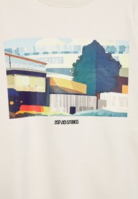 Witte sweatshirt met een kleurrijke, abstracte print van gebouwen en bomen, in blauwe, groene, oranje en gele tinten. "207-213 Studios" onderaan.