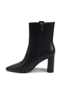 Bottine en cuir noir avec bout pointu, talon bloc et fermeture éclair sur le côté, sur fond blanc.