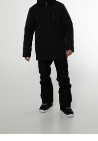 Musta eristetty parka hupulla, kahdella etutaskulla, vetoketjullisella rintataskulla ja säädettävillä hihansuilla. Yhdistetty mustiin housuihin ja mustiin lenkkareihin.