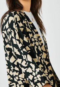 Schwarzer und beiger Kimono mit einem abstrakten geometrischen Muster; leichtes Material; lockere Passform; halb-lange Ärmel; minimale Hardware-Akzente.