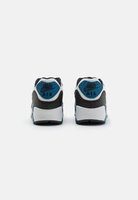 Nike Air-sneakers i svart, vitt och blått. Har en texturerad läderöverdel, vadderat krage och framträdande Nike-logotyp på hälkappan.