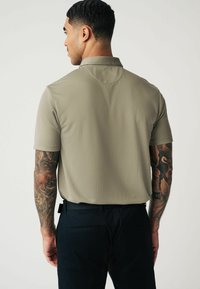 Kurzärmeliges, hellolivgrünes Poloshirt mit strukturiertem Muster, ausgestattet mit einem klassischen Kragen und einem lässigen Schnitt, kombiniert mit dunklen Hosen.