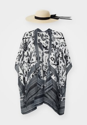 Sombrero de paja de ala ancha con cinta negra y bata de estilo kimono con patrón floral y de pájaros en blanco y negro colgada sobre fondo blanco.