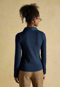 Navy ribbed long-sleeve shirt with a collar and buttoned cuffs, paired with plaid trousers. Textured fabric and fitted silhouette.