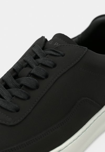 Close-up of a black sneaker with textured black laces and a white rubber sole, showing detailed stitching and smooth upper material.