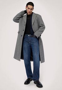 Grå yllekappa med skräddarsydd design, lager-på-lager över en svart topp, kombinerad med blå jeans och svarta stövlar. Dubbelknäppt med stora knappar.