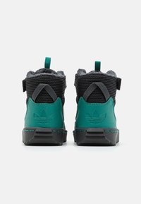 Zapatillas de media caña en verde y negro con tejido texturizado, suela de goma y una lengüeta en la parte trasera; incluye un detalle decorativo de un logo con forma de hoja.