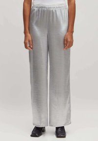 Zilveren, wijde broek gemaakt van een glanzende, gestructureerde stof. De elastische tailleband zorgt voor gemakkelijk draagcomfort. Gemaakt in combinatie met zwarte schoenen.