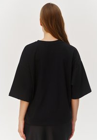 Czarna, oversize koszulka z krótkim rękawem, okrągłym dekoltem, wykonana z miękkiej bawełny. Prosty design, bez widocznych wzorów czy elementów ozdobnych.