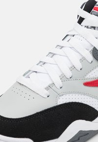 Zapatillas grises y negras con texturas de cuero y ante, cordones blancos, parte superior perforada y detalles en rojo. Diseño de punta redonda.