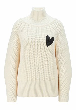 Pull à col roulé en grosse maille crème avec manches longues et petit écusson noir en forme de cœur sur la poitrine gauche.
