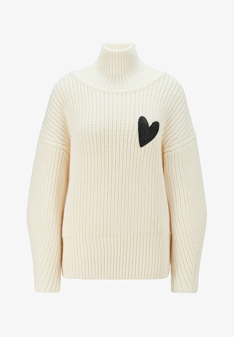 Pull à col roulé en grosse maille crème avec manches longues et petit écusson noir en forme de cœur sur la poitrine gauche.