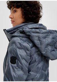 Gepolsterte Bomberjacke in Grau mit hohem Kragen, Reißverschlusstaschen und einem schwarzen Logopatch am linken Ärmel. Glatte, gesteppten Textur.