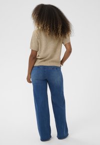 Top in maglia beige a maniche corte con orlo a coste abbinato a jeans a gamba larga blu. Texture liscia, vestibilità casual, design in denim classico, non decorato.