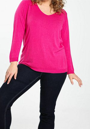 Långärmad rosa stickad tröja med V-ringning och ribbad nederkant, i kombination med mörkblå skinny jeans med kontrasterande sömdetaljer.