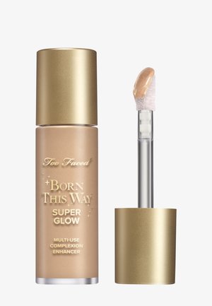 Too Faced Born This Way Super Glow, een glazen fles met een matte gouden dop, bevat een lichtbeige vloeistof met een zachte borstelapplicator.