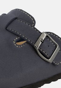 Marine suède sandaal met een brede band voorzien van een zilveren metalen gesp en contrasterende stiksels, textuurovervlak en een platte zwarte zool.