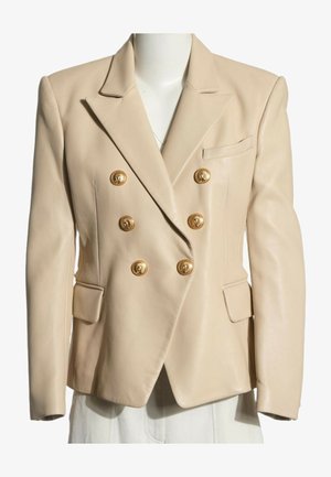 Blazer beige de doble botonadura con seis botones decorativos dorados y dos bolsillos delanteros con solapa en el torso de un maniquí.