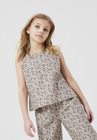 Ljust beige ärmlös topp och matchande byxor, båda med små mörka blommönster, med lös passform och mjuk textur.