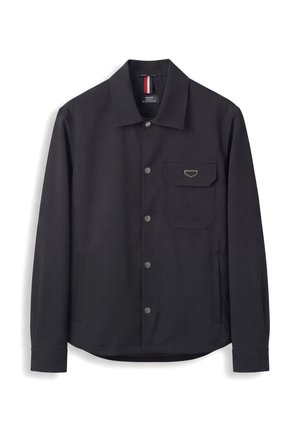 Camisa negra de manga larga con botones a presión metálicos, cuello puntiagudo y un bolsillo en el pecho con solapa y detalle metálico.