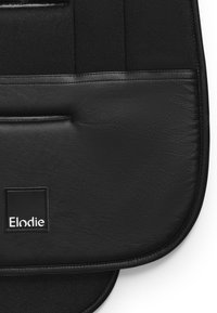 Svart vadderad tyg med texturerade läderdetaljer; har en liten fyrkantig logo som läser "Elodie" och en dragkedjeficka.
