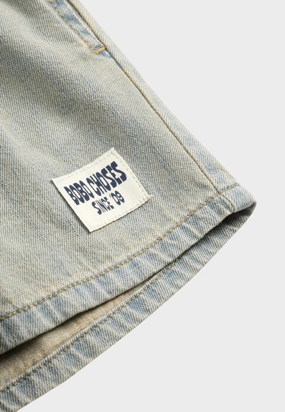 Light blue denim fabric with a white rectangular label stitched near the edge, displaying "BOBO CHOSES SINCE '09" in dark blue text.