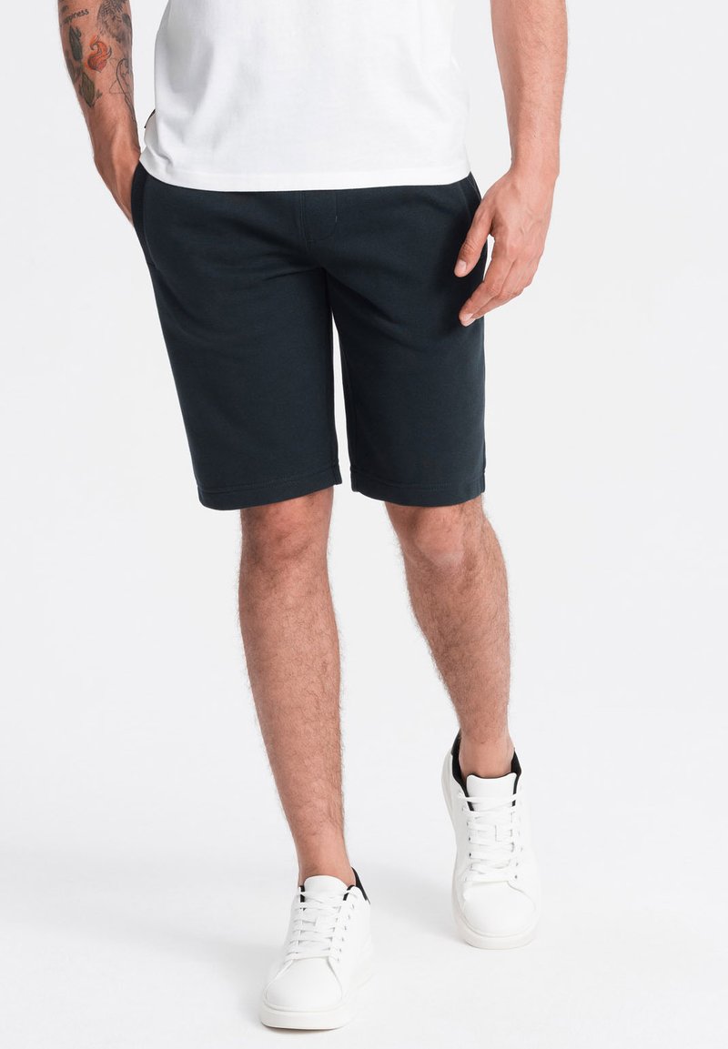 Shorts noirs en coton avec une coupe décontractée, poches latérales et ceinture plate. Assortis à des baskets blanches avec des accents noirs.