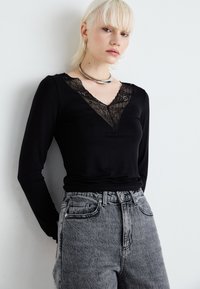 Top negru cu mânecă lungă, cu o decolteu în formă de V din dantelă, asociat cu blugi din denim gri cu talie înaltă. Material neted și croială ajustată.