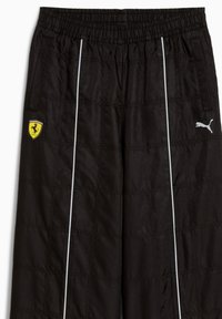 Pantalons de sport noirs en tissu léger, dotés d'un logo Ferrari et d'un logo Puma, avec des bandes blanches sur les côtés et une taille élastique.