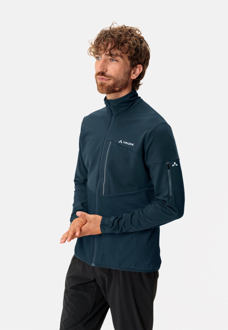 Donker teal lange mouwen jack met hoge kraag, voorzak met rits, gestructureerd onderste gedeelte en logo op de borst en mouw.