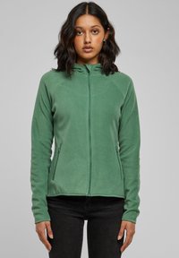 Žalias fliso užtrauktuku užsegamas švarkelis su aukštu apykakliu, ilgomis rankovėmis ir šoniniais kišenėmis, pasižymintis lygiu paviršiumi ir pritaikytu dizainu.