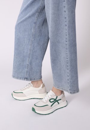 White and light grey sneakers with green accents, mesh and suede materials, round toe, and contrasting laces, paired with light blue wide jeans.