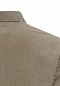 Brun kordfløjlsskjorte med vertikal ribbet tekstur og krave, med en glat finish og et diskret design. Ingen synlig hardware eller detaljer.