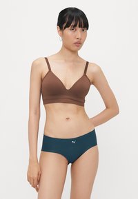 Bralette castanho sem costuras com alças ajustáveis, combinado com calções de bikini verde-água com um pequeno logotipo branco na frente. Textura suave, design minimalista.