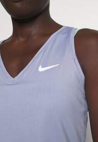 Camiseta deportiva sin mangas de Nike en color lavanda claro con diseño de cuello en V, con un logo blanco y tela texturizada.