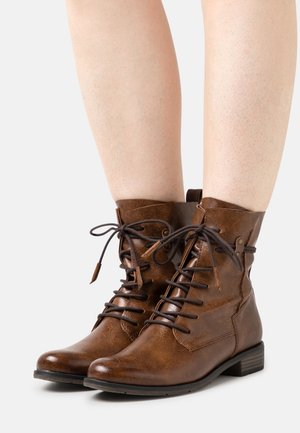 Bottes montantes en cuir marron avec bout rond, fermeture à lacets et détails métalliques. Présentent une finition texturée et un petit talon empilé.