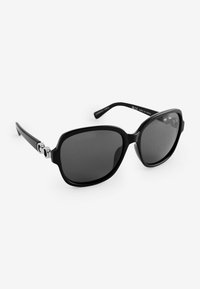 Gafas de sol negras con un armazón cuadrado sobredimensionado, lentes oscuros y acabado brillante; presenta acentos de metal plateado en las patillas.