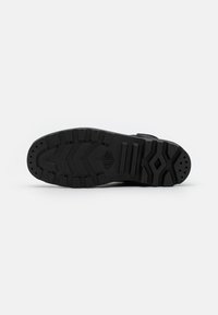 Suola di scarpa in gomma nera con un motivo di battistrada caratterizzato da scanalature, creste e fori di ventilazione circolari. Design robusto adatto per la trazione.