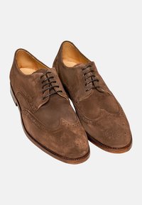 Braune Wildleder-Oxford-Schuhe mit Brogue-Verzierungen, runder Zehenform, Schnürung und Innenfutter aus hellbraunem Leder. Die Sohle hat eine glatte Oberfläche.