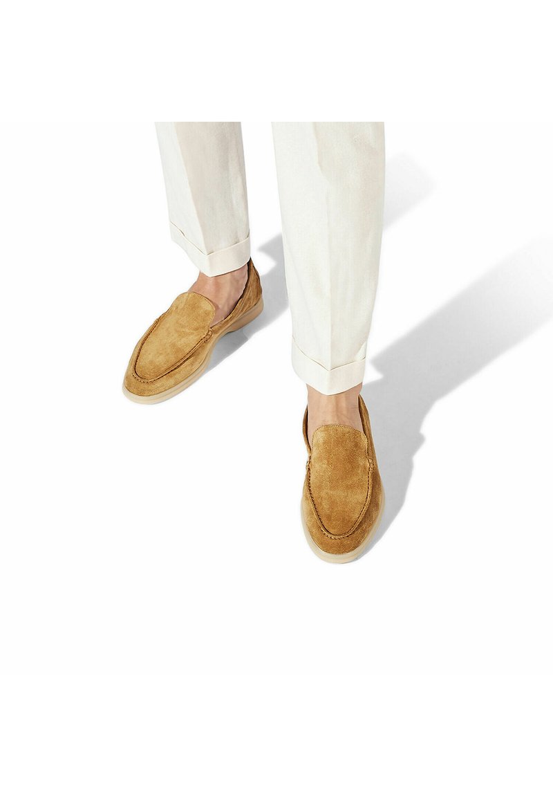 Scarpe slip-on in suede color cammello con punta arrotondata, texture morbida, cuciture in contrasto e suola leggera e flessibile. Indossate con pantaloni chiari.