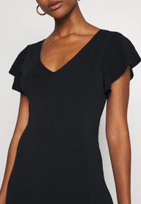 Robe noire côtelée avec un décolleté en V et de courtes manches à volants. Texture lisse et silhouette ajustée, idéale pour un style polyvalent.