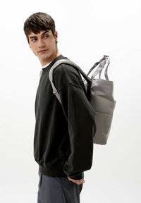 Grå ryggsäck med en strukturerad design och texturerad yta, bärs över en svart sweatshirt, med dubbla randiga axelremmar.