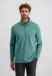 Lichtgroene lange mouwen pullover met een halve ritssluiting bij de kraag. Soepele textuur en aansluitend ontwerp, met een subtiele logo op de borst.