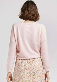 Pull en tricot rose clair avec une coupe décontractée et des poignets côtelés, associé à une jupe florale à motifs avec des accents roses et dorés.