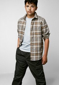 Rutig flanellskjorta i beige och brunt över en ljusgrå t-shirt, kombinerad med svarta cargobyxor med sidofickor och avslappnad passform.