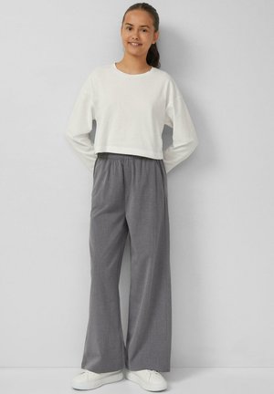 Cropped witte sweatshirt met lange mouwen, gecombineerd met grijze wijde broek met een elastische tailleband, gedragen met witte sneakers.
